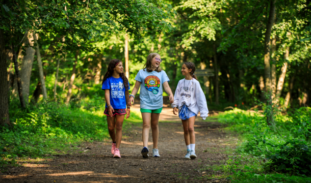 three girl scouts walking on hiking path in wooded area 