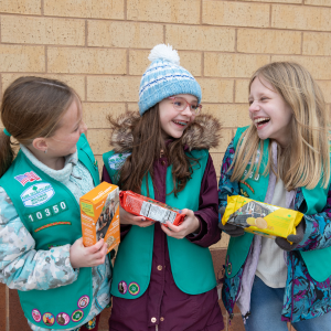 three girl scout juniors holding cookies and laughing
