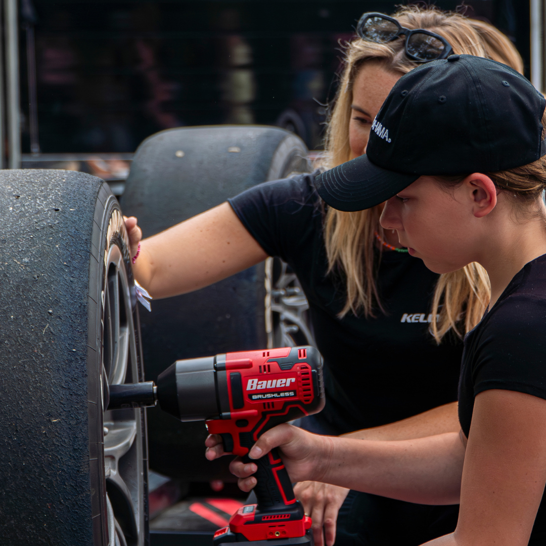 female mechanic helping girl scout install tire