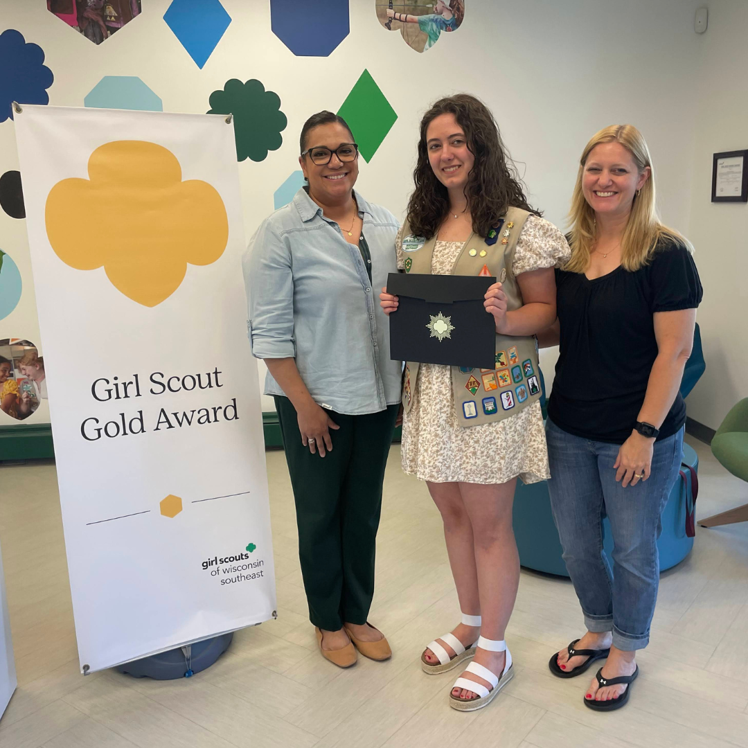 gold award girl scout posing with certificate and ceo and mom