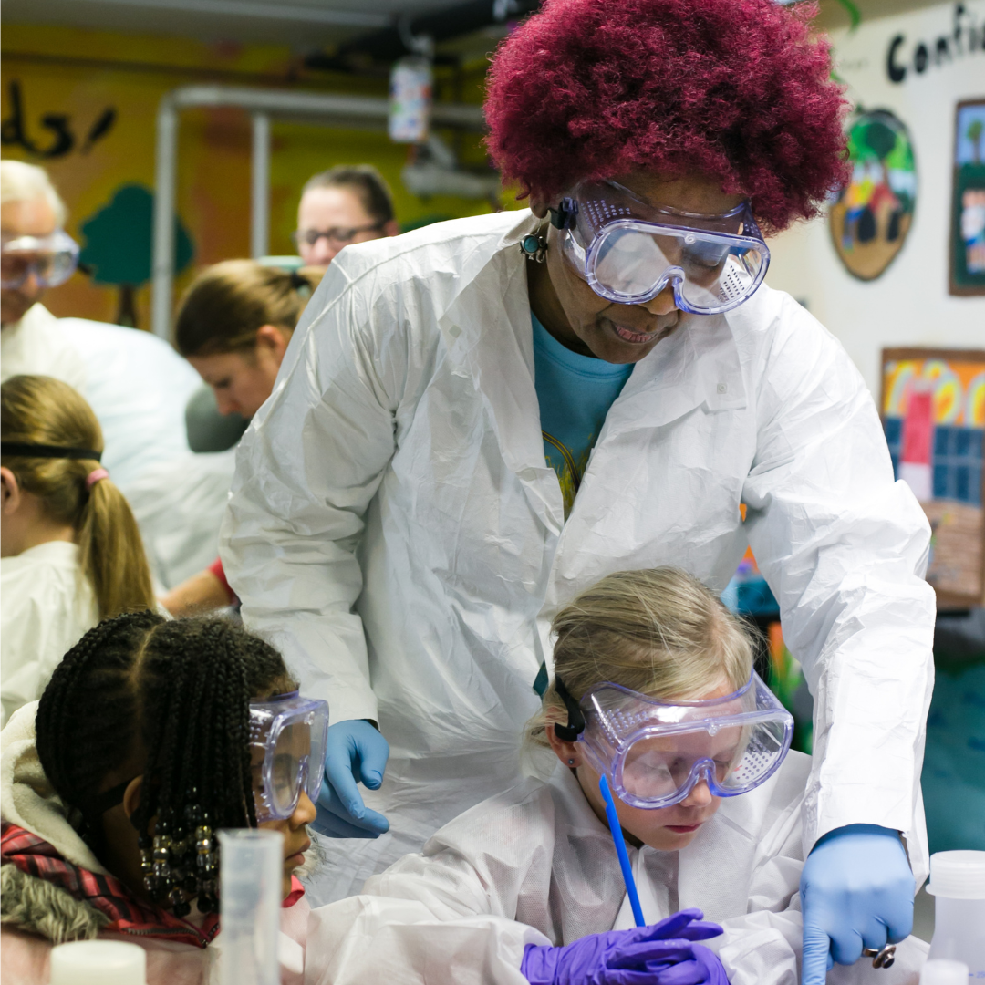 girl scout volunteer and two girl scouts in lab goggles and white coats working on stem project
