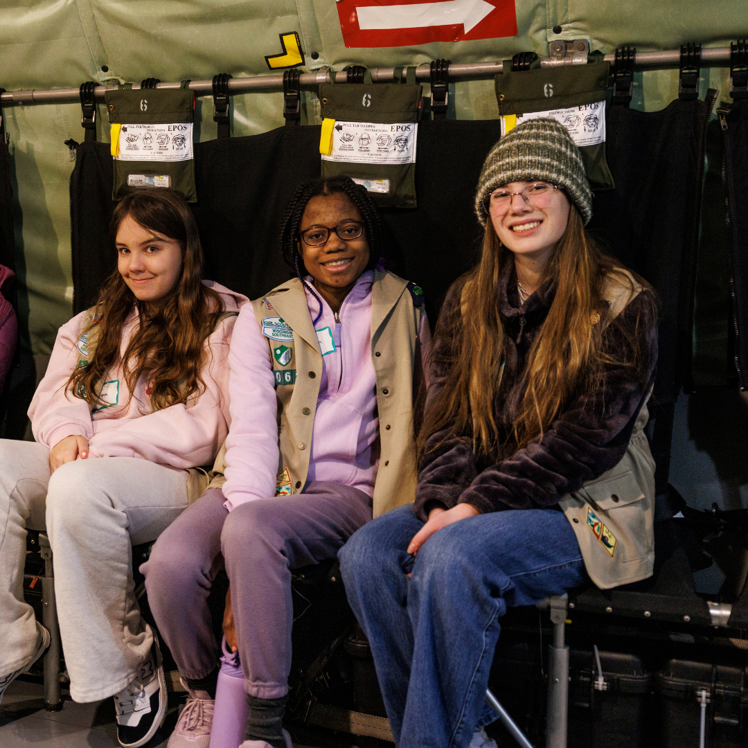three girl scouts sitting in interior of military plane