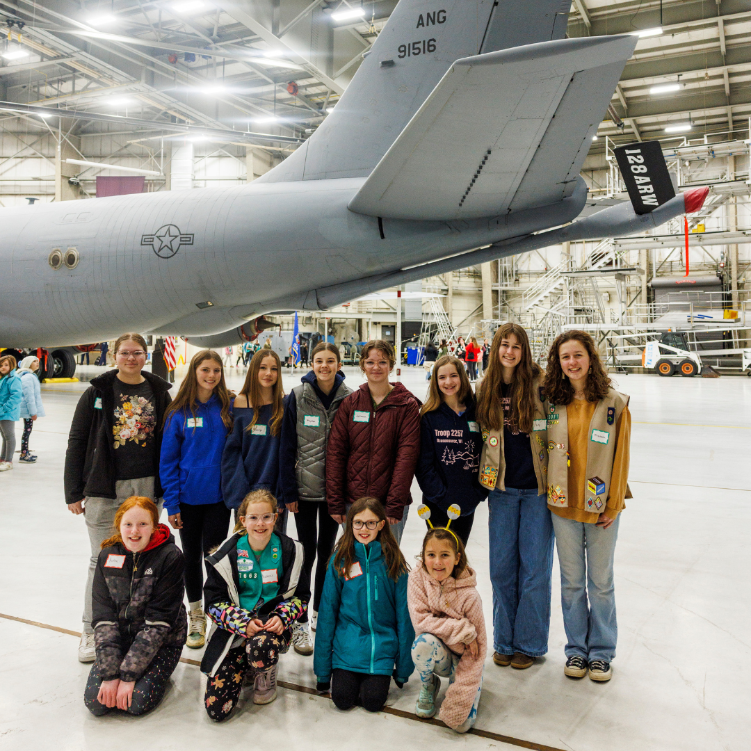 large troop of girl scouts in front of military plane in hangar
