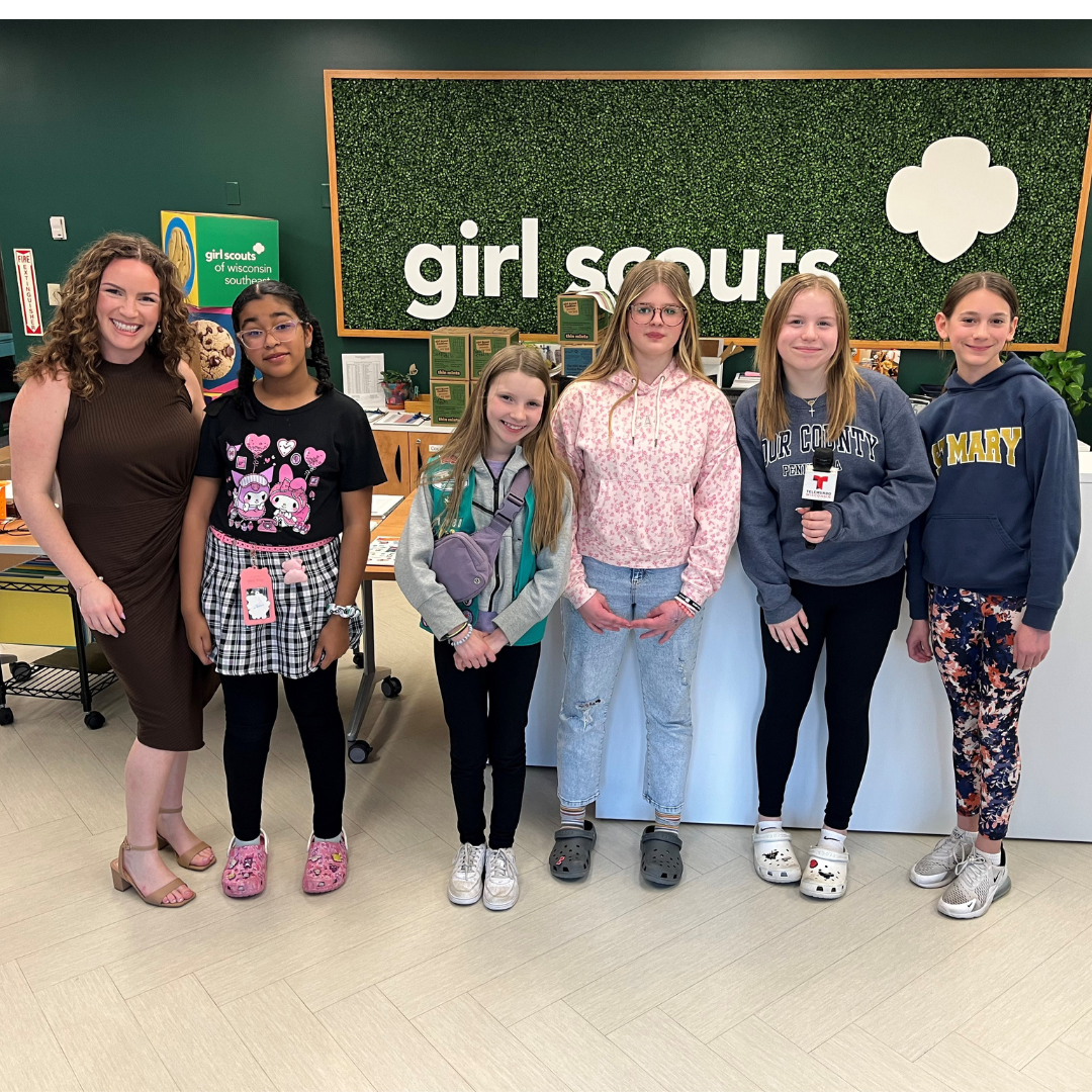 girl scouts in front of green wall holding microphone with tv reporter