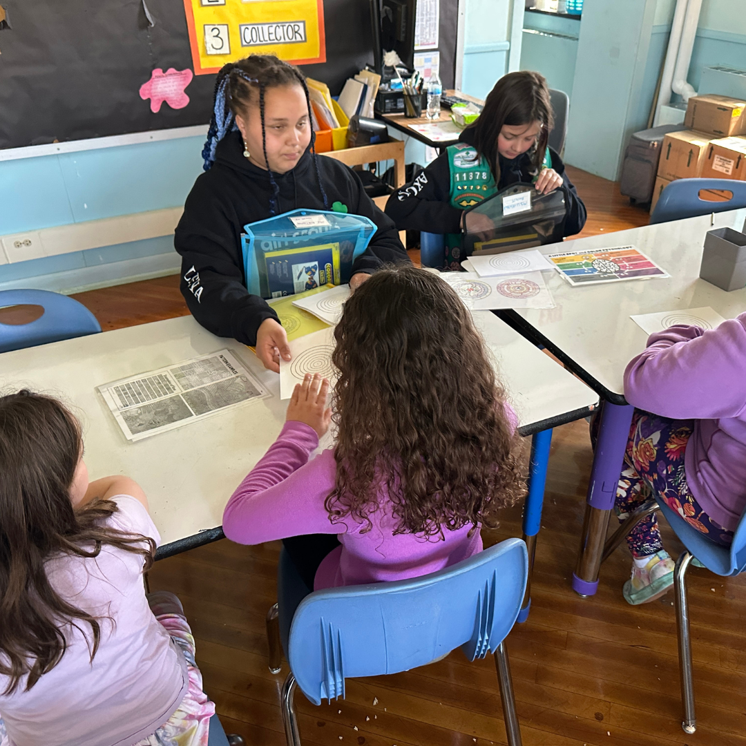 two girl scouts helping two other classmates with art kits