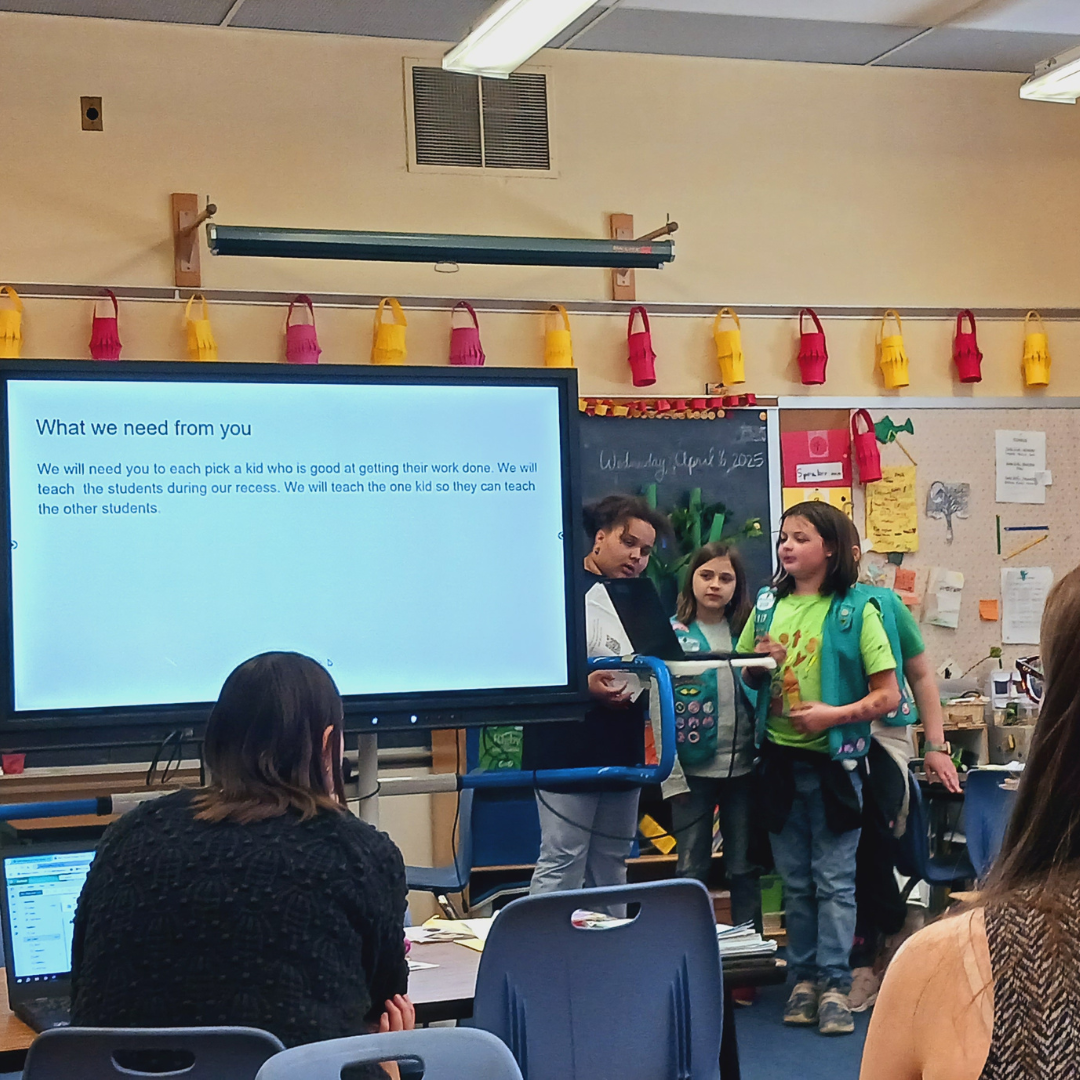 junior girl scouts presenting powerpoint to teachers at front of classroom