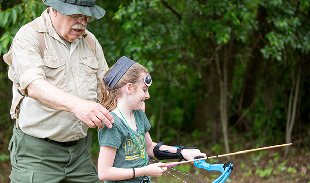adult volunteer helping Girl Scout during archery lesson