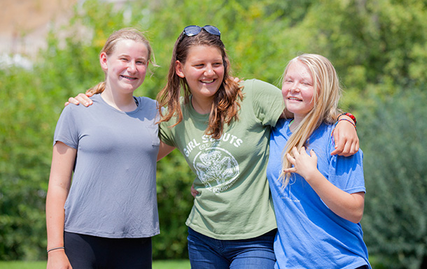 three older Girl Scouts hugging and smiling