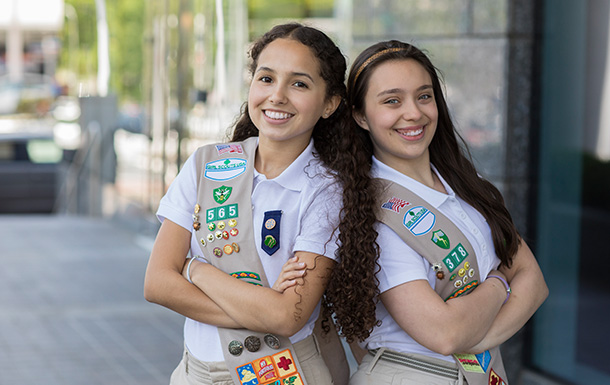 Two Girl Scouts with arms crossed and smiling at the camera in Girl Scout sashes