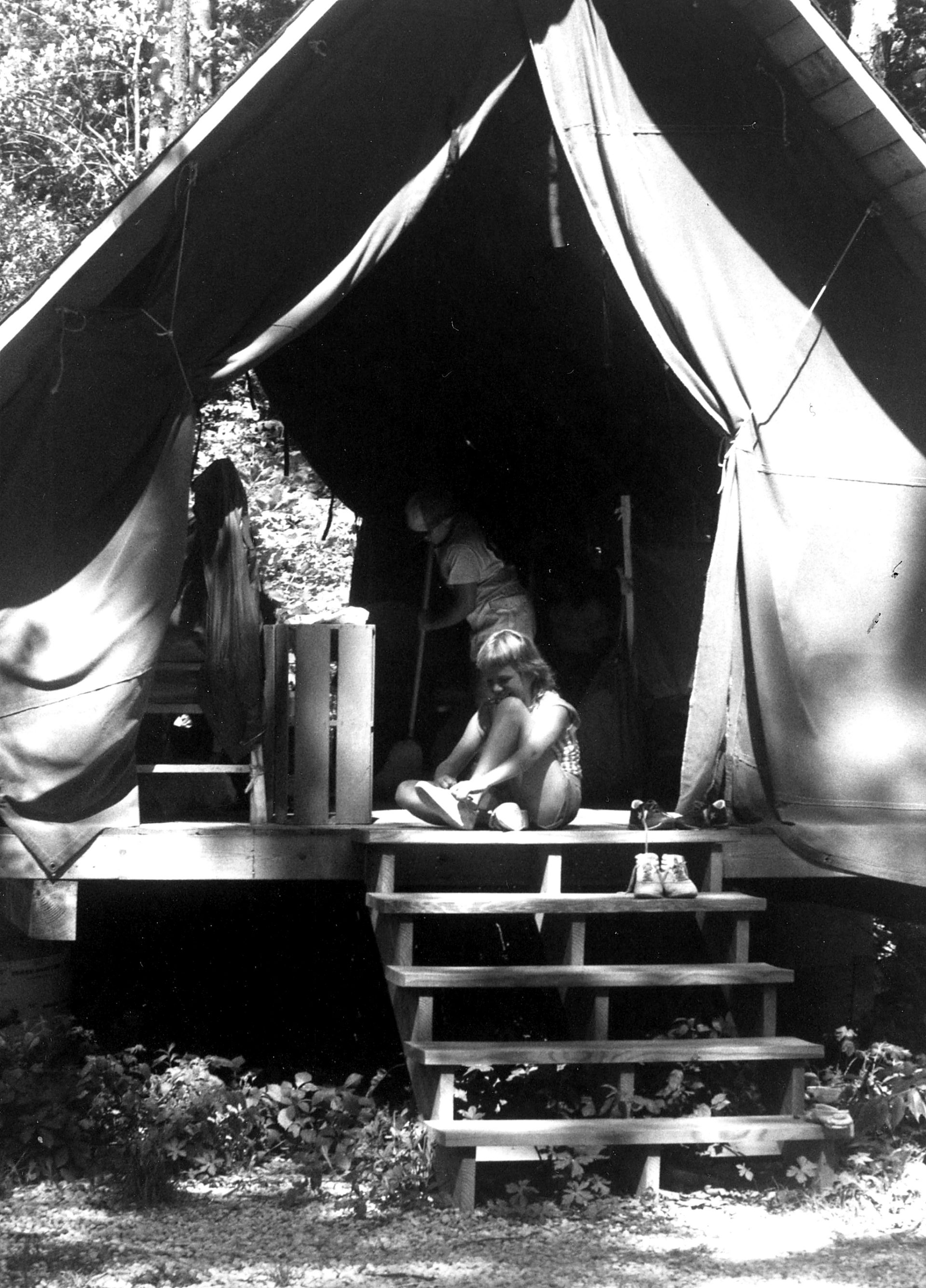 vintage black and white photo of girl scout putting on shoes in platform tent