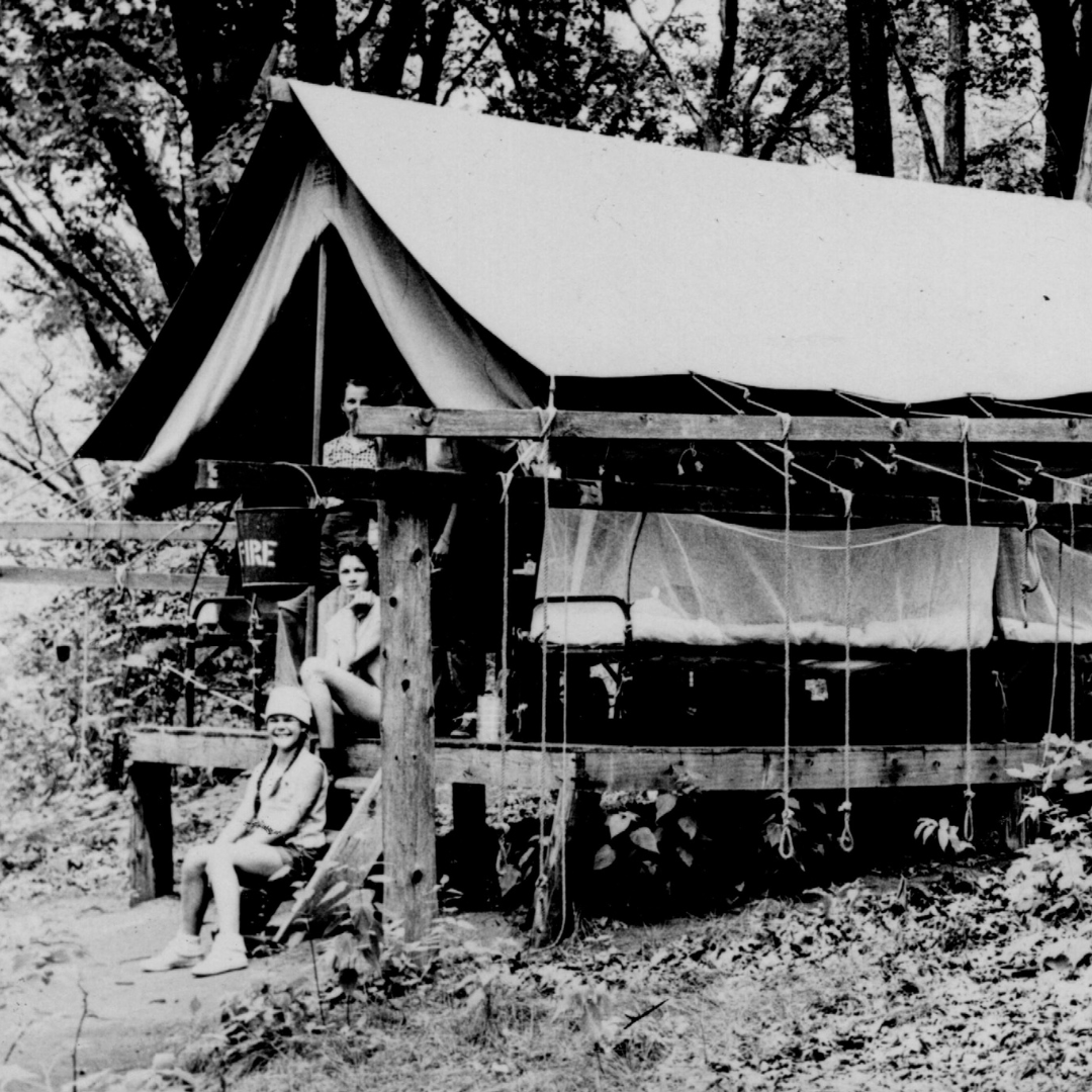 vintage black and white photo of campers posing in front of platform tent
