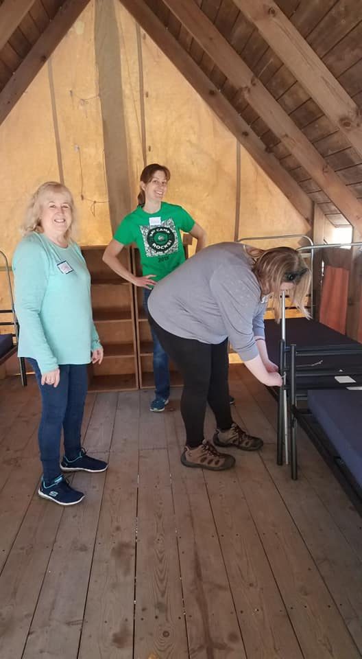 Three women stand inside a platform tent at Camp Alice Chester. Andrea Yanacheck poses in middle of the group.