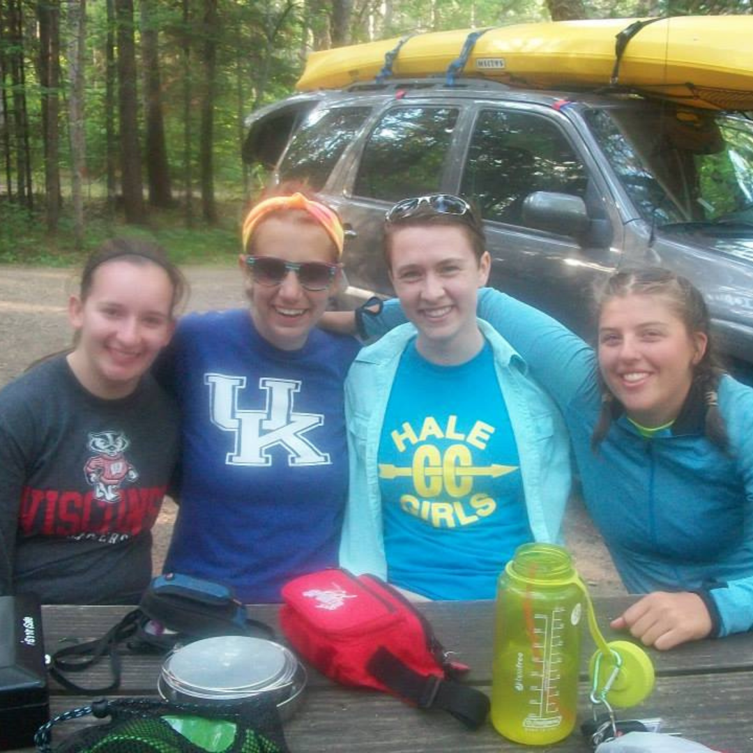 four campers sitting at picnic table in front of kayak