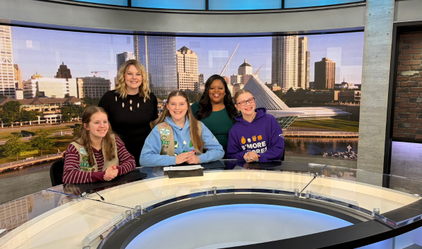 three girl scouts at news desk with two reporters