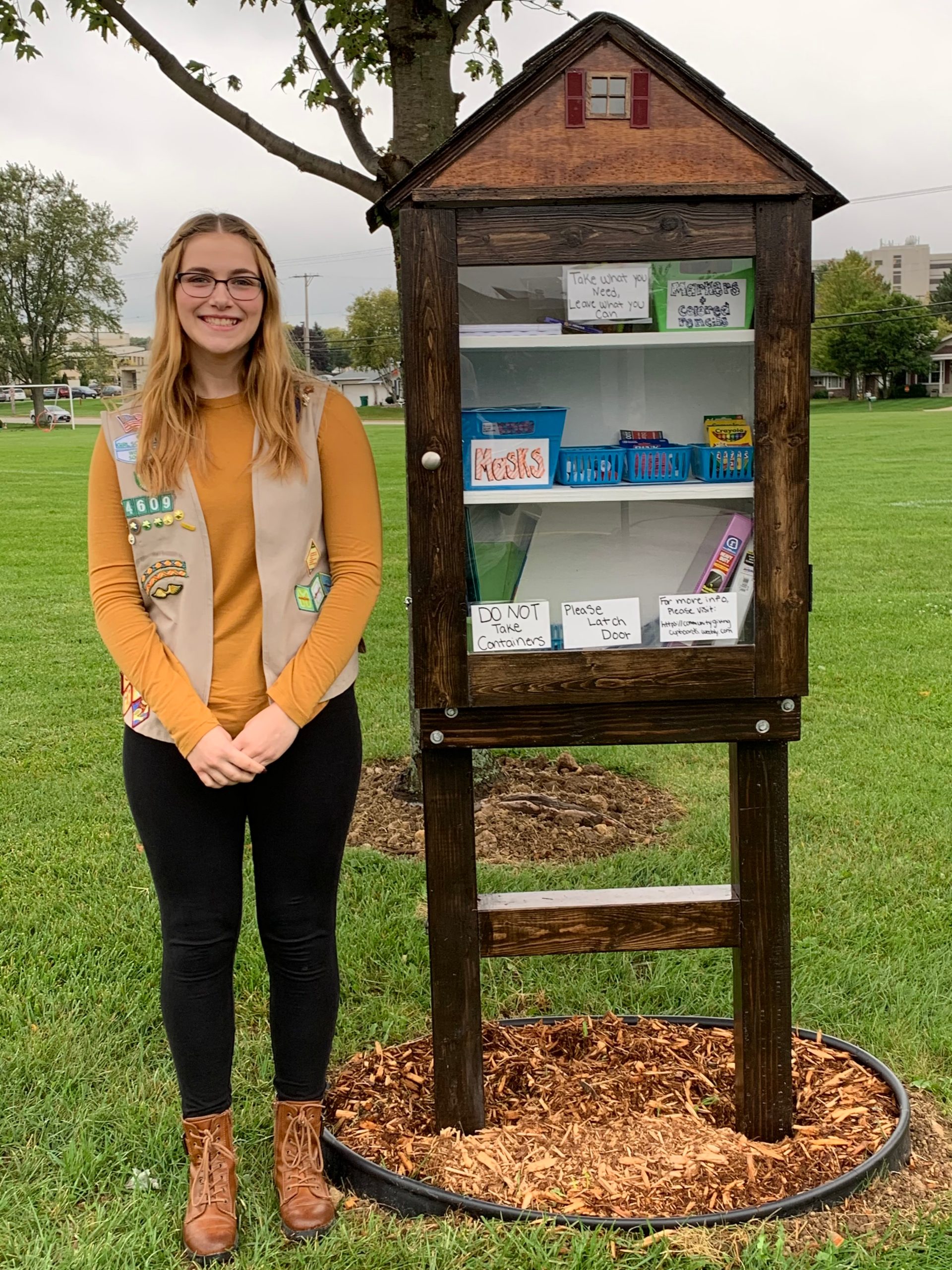 Gold Award Girl Scout standing proudly next to community cupboards she built
