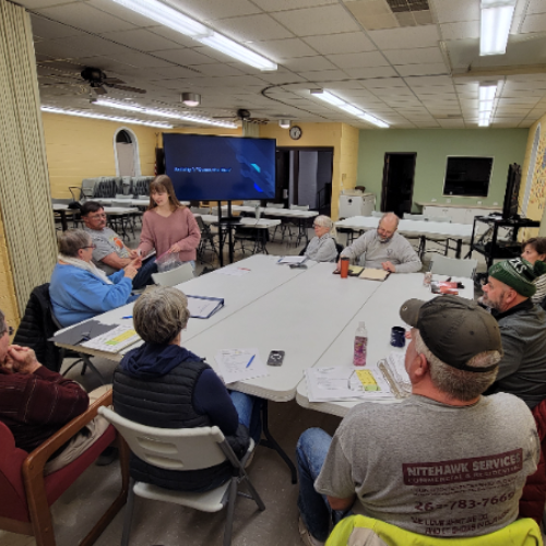girl scout with presentation in front of group of people seated around table