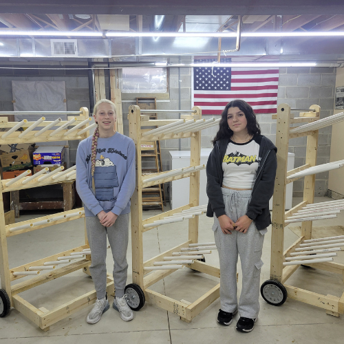 two girl scouts standing in front of shoe racks in woodworking shop