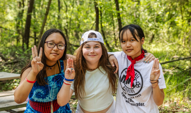 three girl scouts at summer camp holding girl scout promise sign
