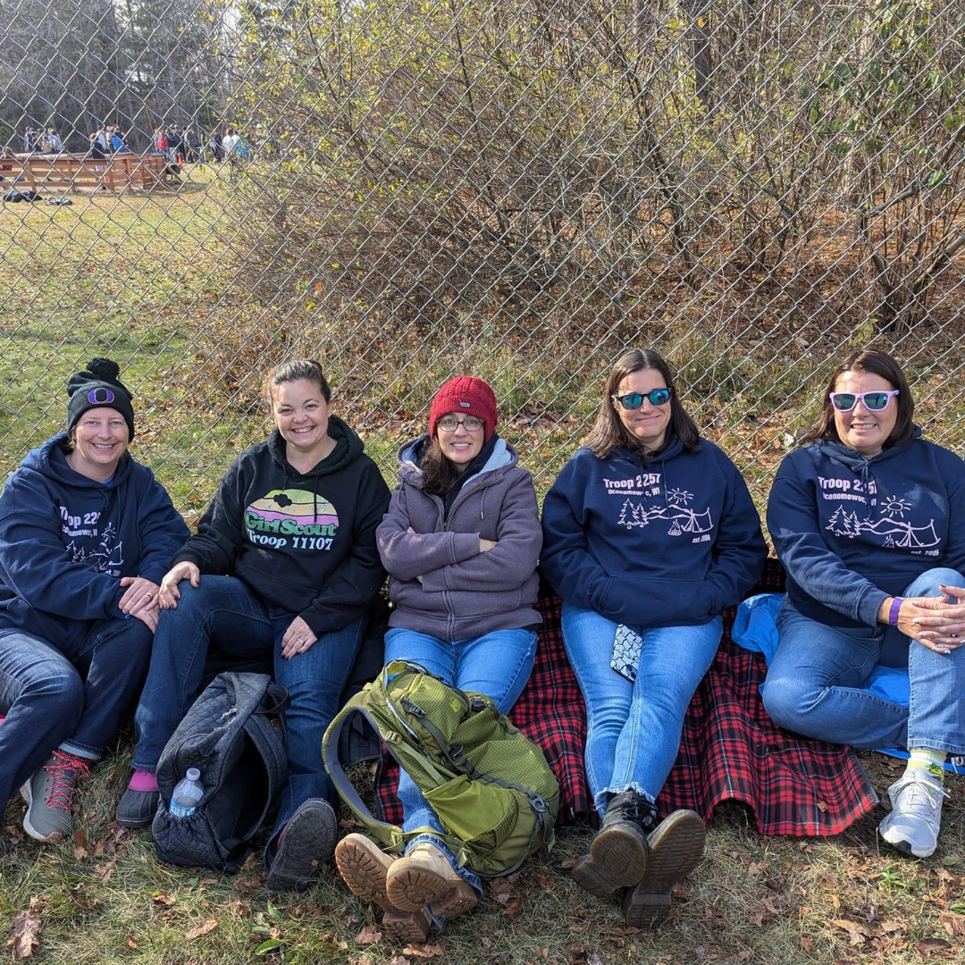 girl scout troop leaders sitting in front of outdoor fence