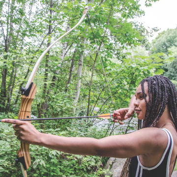 Young woman shooting bow and arrow in forest